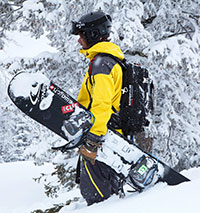  man carrying snow-covered snowboard in knee deep snow