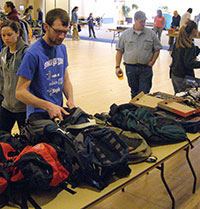 man looking at backpacks on a table with other people walking around