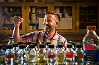 man in lab with bottles of colorful liquid in front of him
