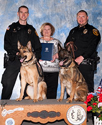 two German shepherd dogs held by two policemen posing with a woman holding certificates