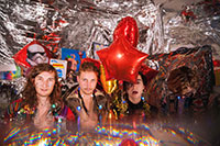 four people posing with shiny balloons and foil everywhere