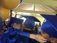 small children in blue caps and gowns hugging with ballons overhead