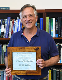 man standing in front of book shleves and holding plaque