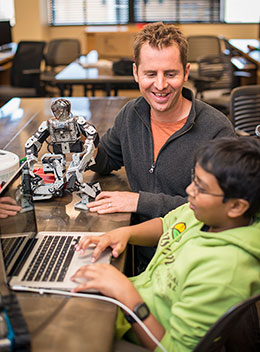 man with small robot talking to boy at computer keyboard