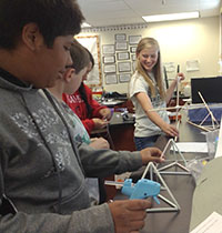 middle school students using glue guns and plastic tubes to build things at a table.