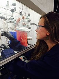 woman working with chemical glassware behind protective glass barrier