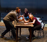 man and woman arm wrestling at table with other people in the background