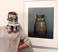 man in a paper owl mask beside a print of an owl