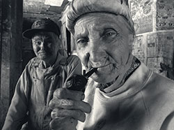 black and white photo of someone smoking a pipe with another person in the background