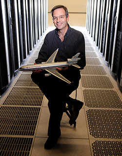 man sitting between rows of computer servers, holding a model airplane