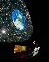 man at planetarium control computer with projection of space overhead