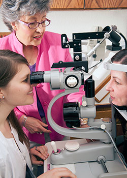 woman supervising another woman using equipment to examine a third woman's eyes