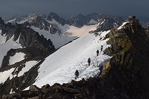 people on a omountianside covered in snow with mountains in background