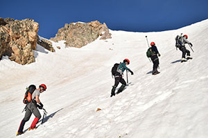 four people climbing up a mountainside covered in snow