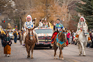 Native Americans in traditional clothing on horseback in front of car