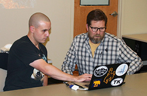 two men seated at a table looking at a laptop computer