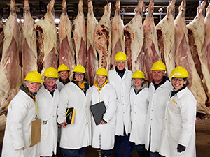 people in hard hats and white coats standing with hanging meat behind them