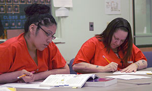 two women in orange jumpsuits studying at a table