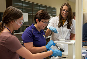 Two teenage girls working with a woman in a lab