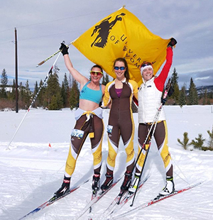 three women on skis holding a University of Wyoming flag