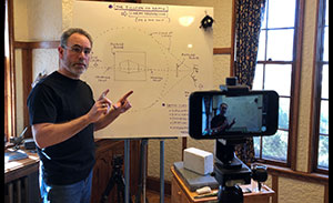 man using cell phone camera to record himself teaching with whiteboard