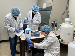 three people in lab protective gear produce hand sanitizer