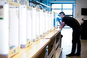 person looking at a 3D printer in a long row of 3D printers