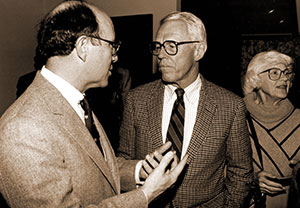 black and white photo of two men talking with a woman in the background