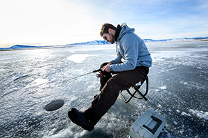 man sitting on stool beside hole in the ice