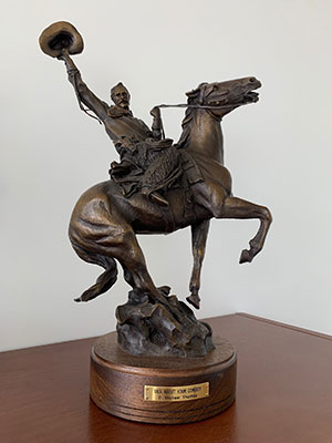 bronze statue of a cowboy on a prancing horse waving his hat