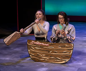 woman and man on a stage with a prop boat and paddle