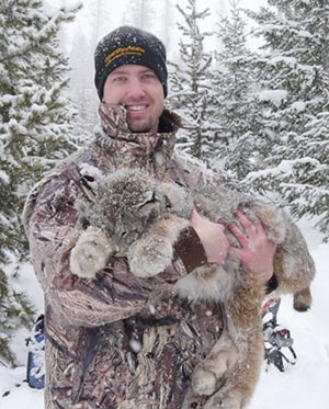 man standing in the snow holding a sedated lynx