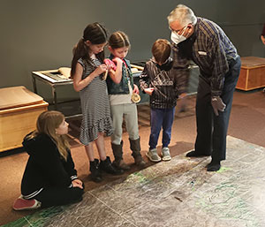 man with several children looking at a large floor puzzle