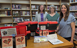 three people standing at a table with black and red plastic boxes and cookbooks