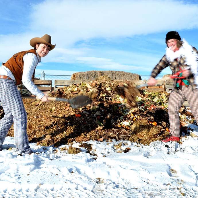 two students shoveling compost in glamorous cowboy outfits