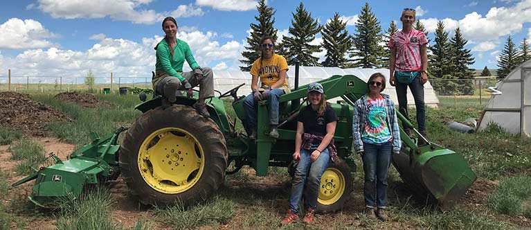 A group of student interns pose on and around the farm's John Deere tractor.