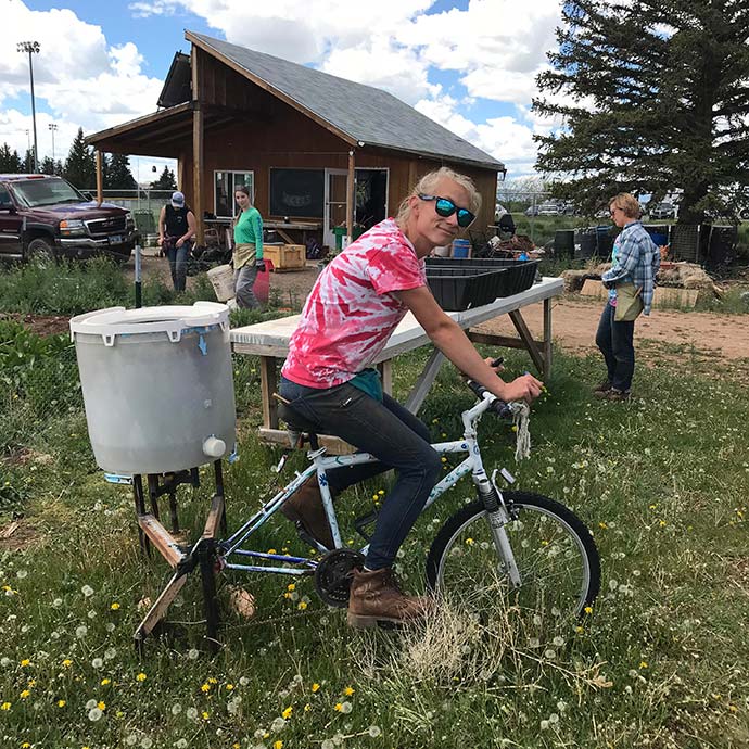 ACRES Farm Manager riding the bicycle-powered salad spinner