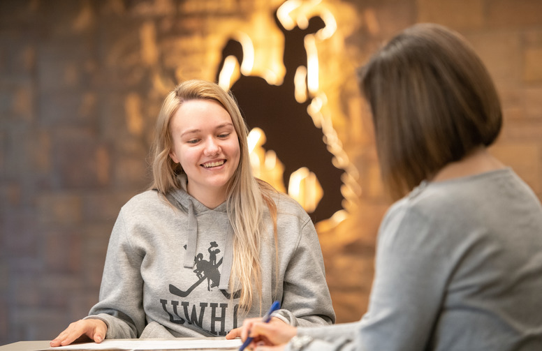 A student speaks with a faculty member in a grey shirt.