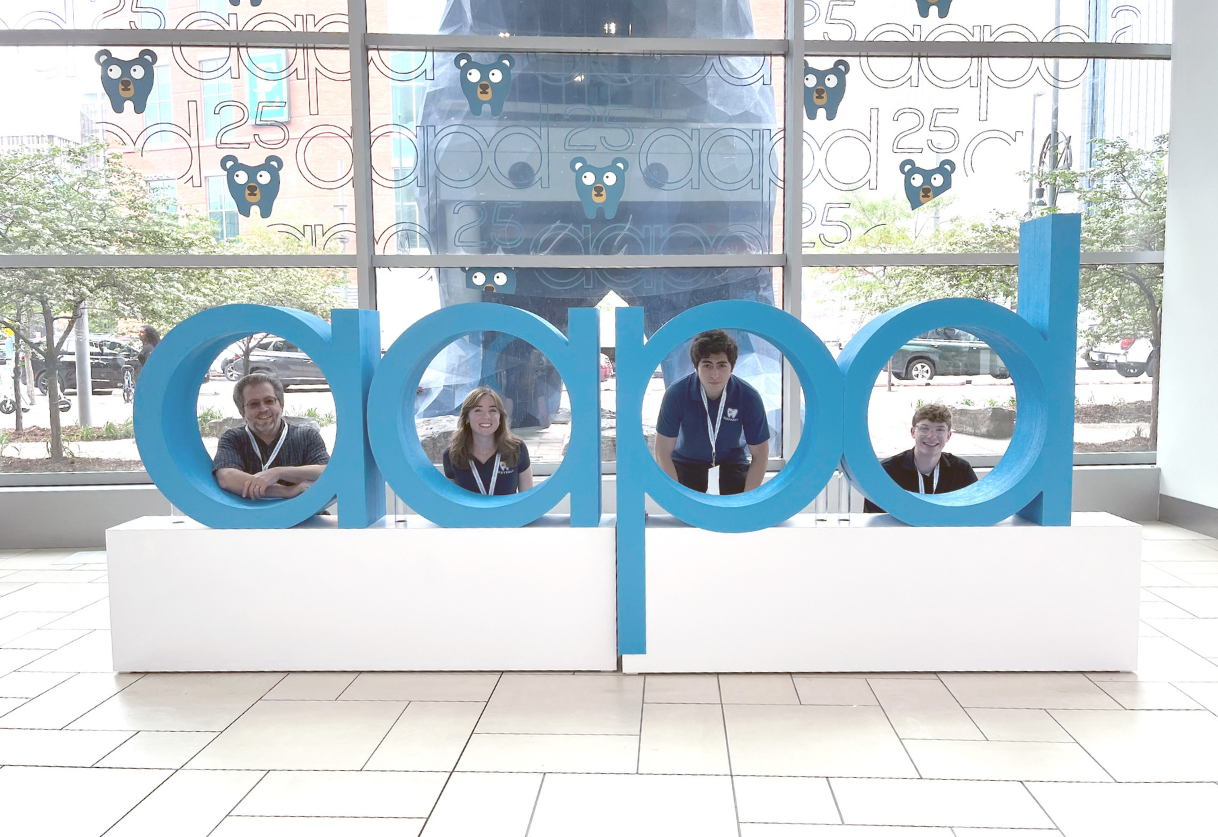 students at dental conference standing behind large blue letters - AAPD