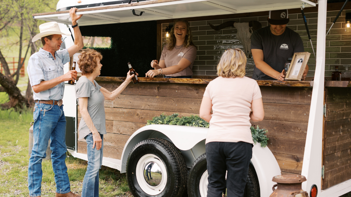 Horse trailer converted to mobile bar, with people getting drinks