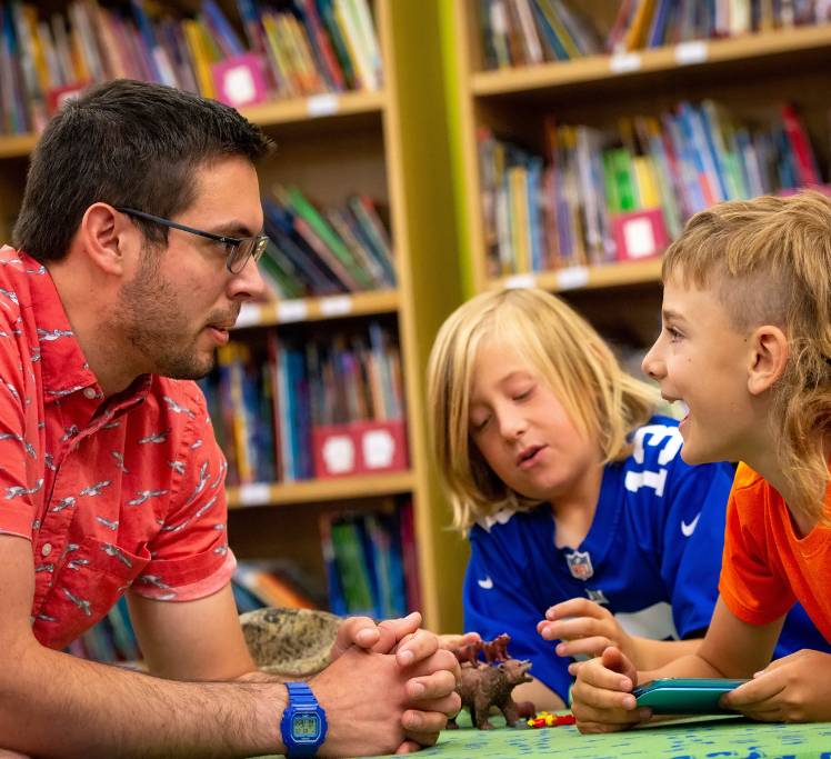 Students playing with dinosaurs next to teacher