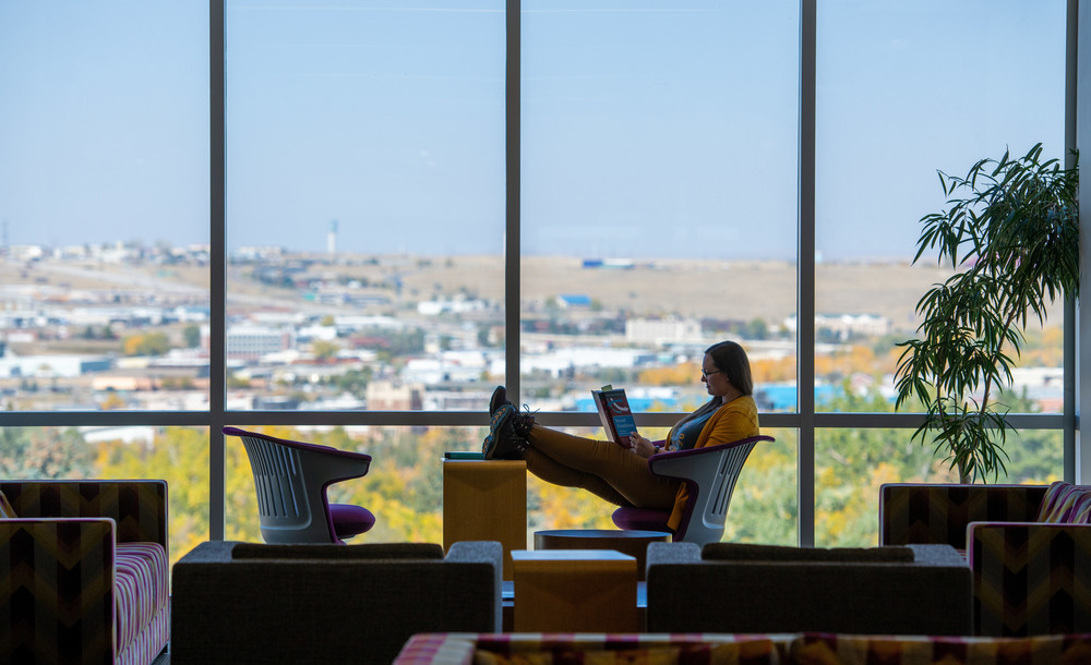 student looks out large windows while reading