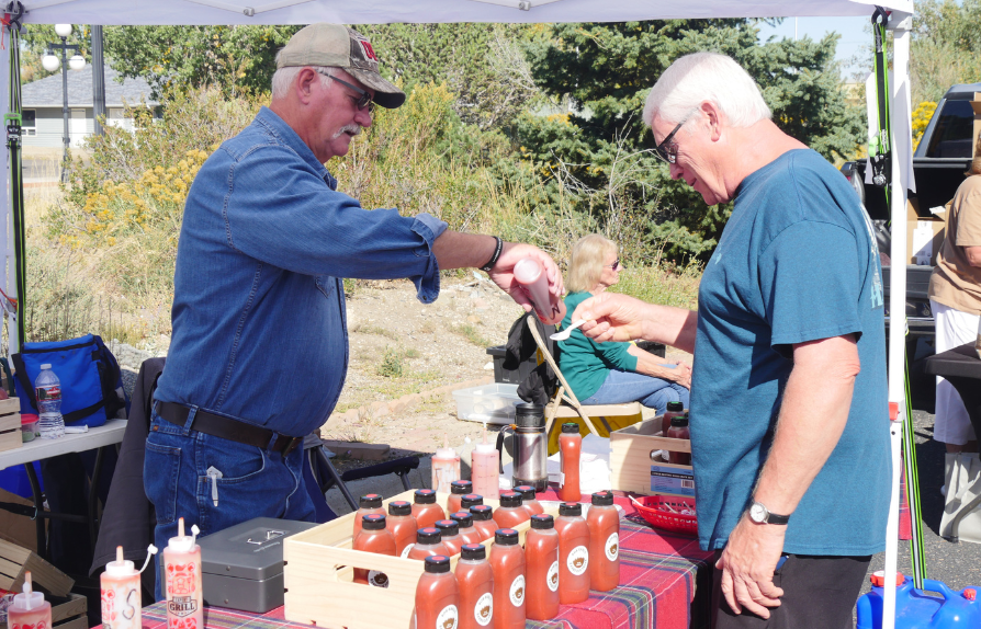a person at a farmers market booth offers a customer a taste of BBQ sauce on a spoon