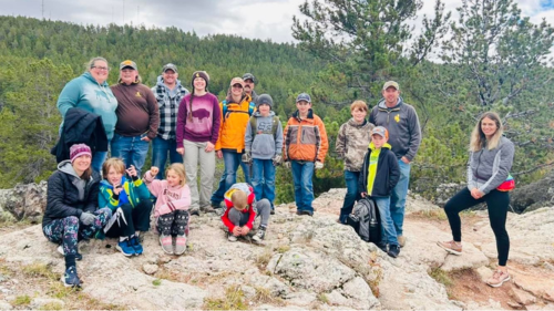 a group of youth and adults poses for a photo on a rock outcrop during a hike