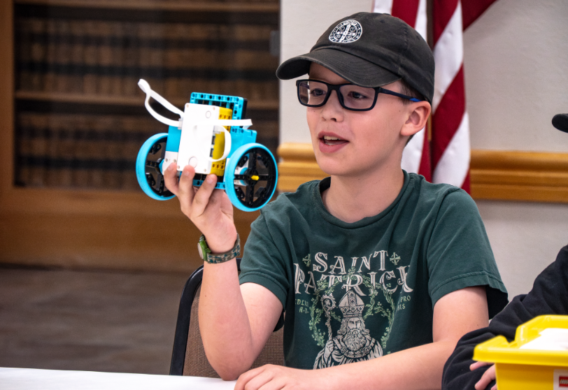 4-H participant holds up a small robot during a hands-on robotics activity.