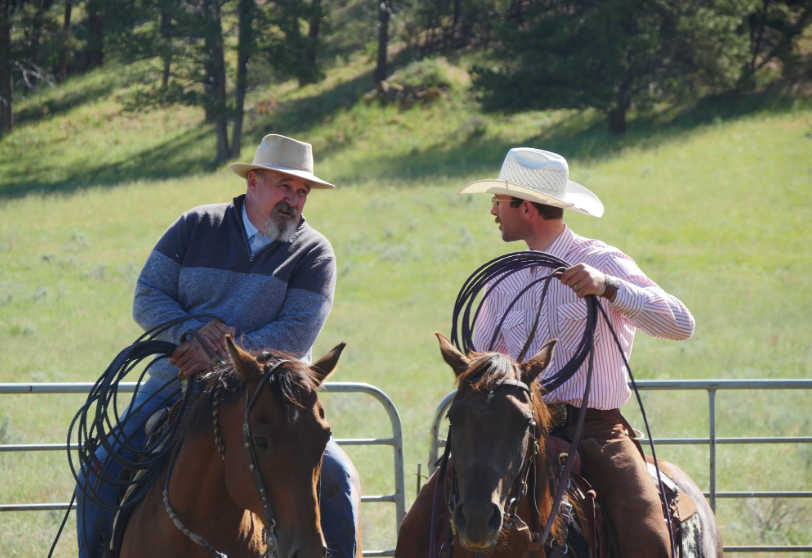 Two riders on horseback hold coiled ropes while talking during a ranch activity.