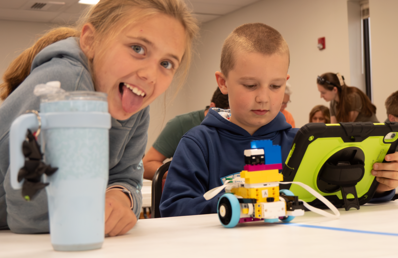 Two 4-H participants work with a small robot and tablet during a hands-on robotics activity.