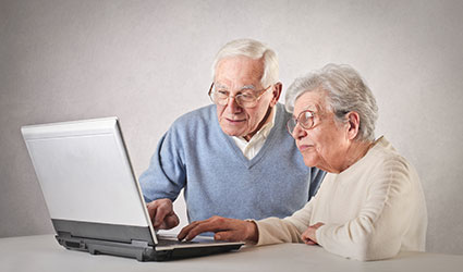An older man and woman work on a laptop together