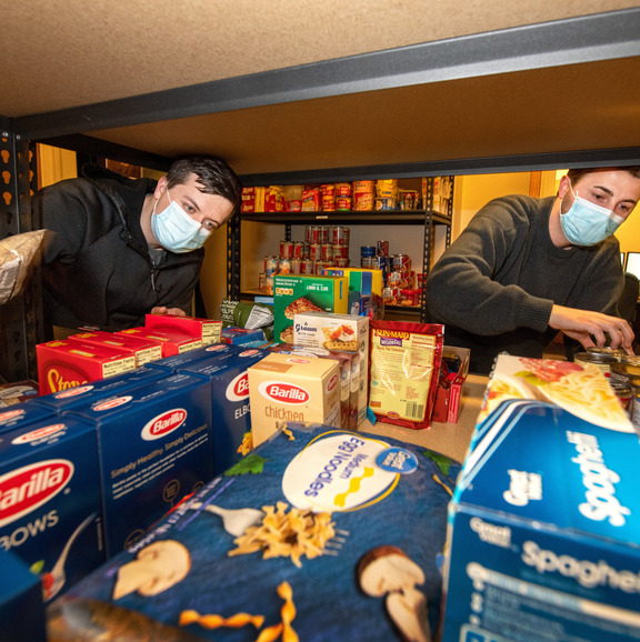 Two people stocking food on a shelf. 