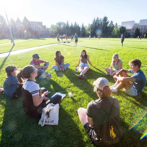 Group of students sitting in a circle on prexi's pasture. 